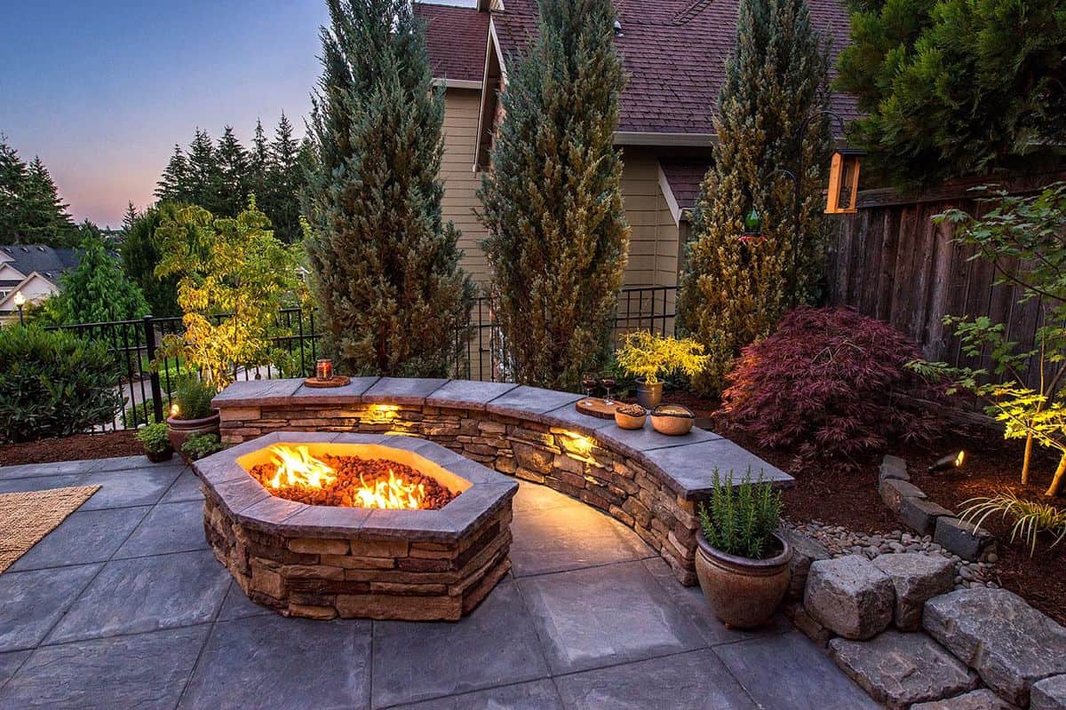 a landscaped patio with built-in stone seating and a circular firepit in the middle
