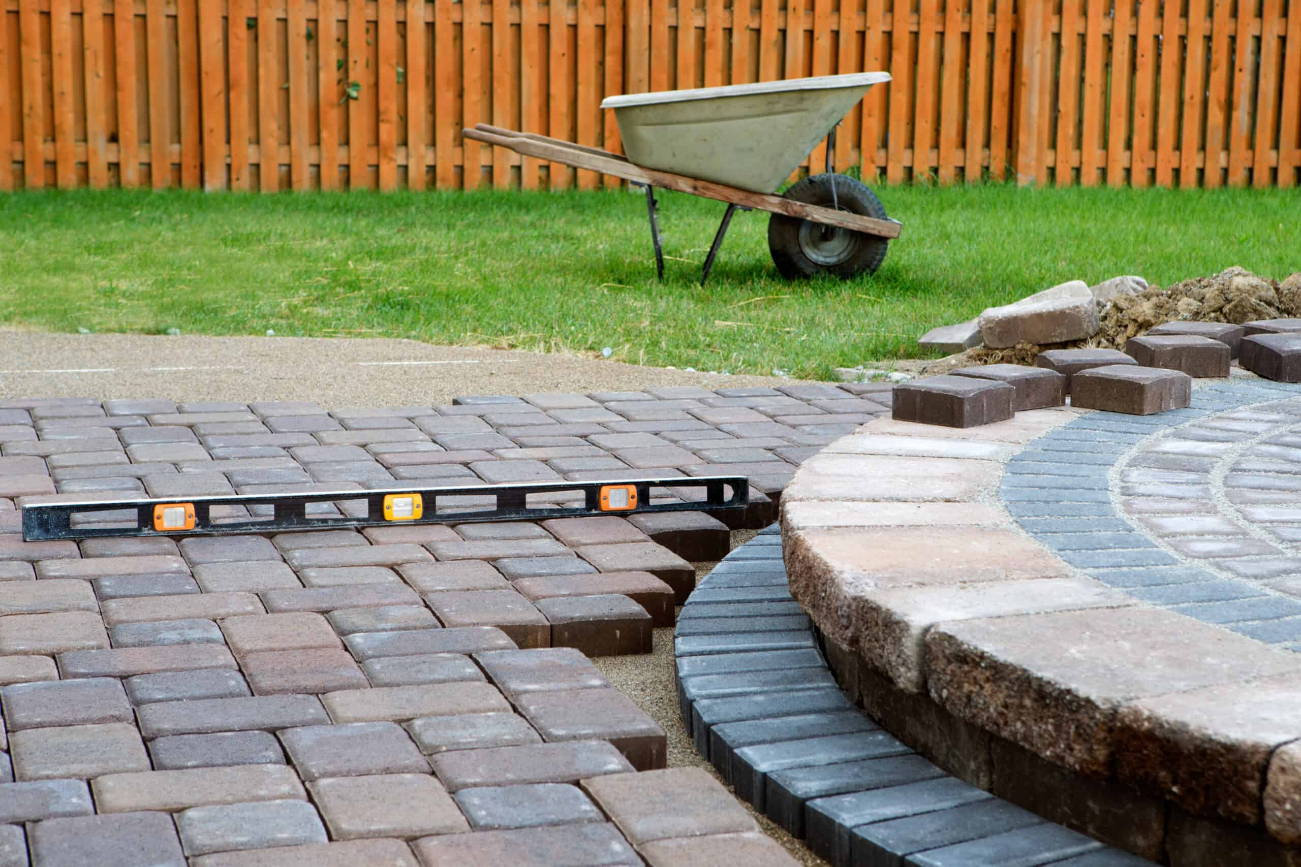 a stone a brick patio firepit under construction with a level and a wheelbarrow in the background