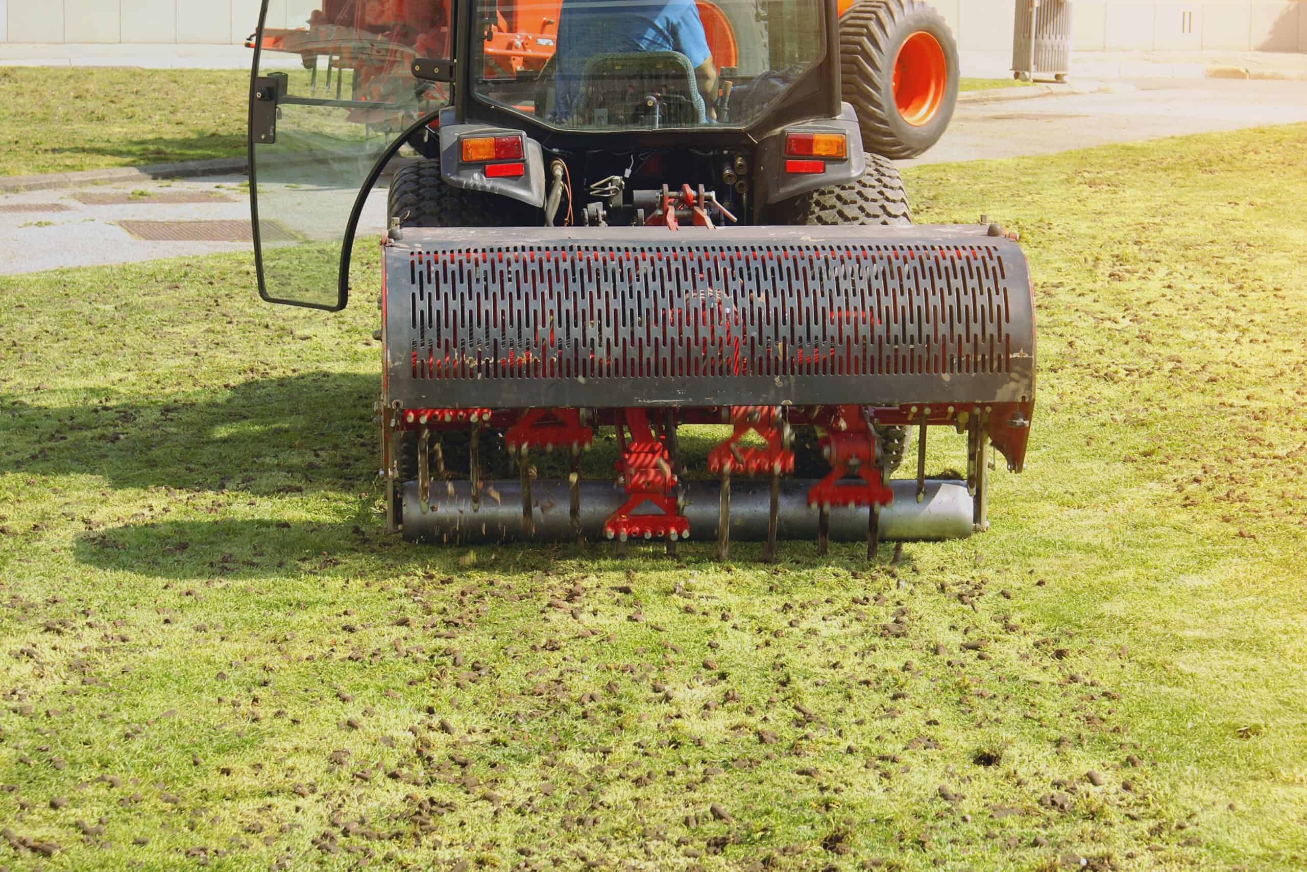 a red aeration machine moving through the grass on a large lawn